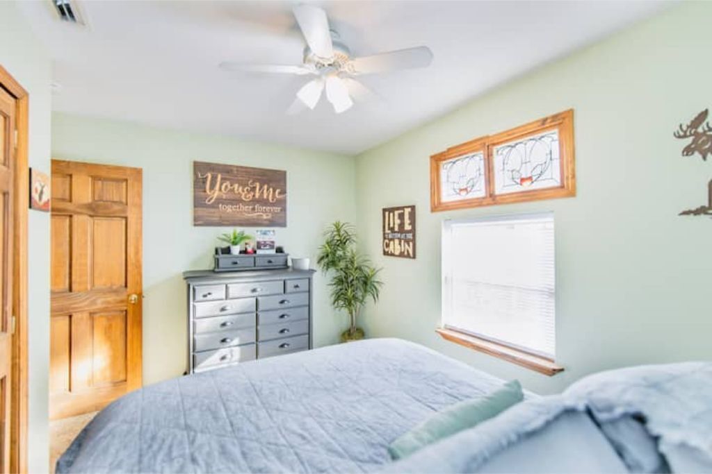 Quarto com cama, penteadeira, ventilador de teto e detalhes decorativos nas paredes.