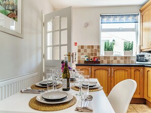 A dining area with a table set for four, including wine glasses, plates, and cutlery. A bottle of wine is on the table, and there is a view of the kitchen and a window with blinds. - 2 bedroom accommodation in Rothbury, near Alnwick (Rothbury, near Alnwick)