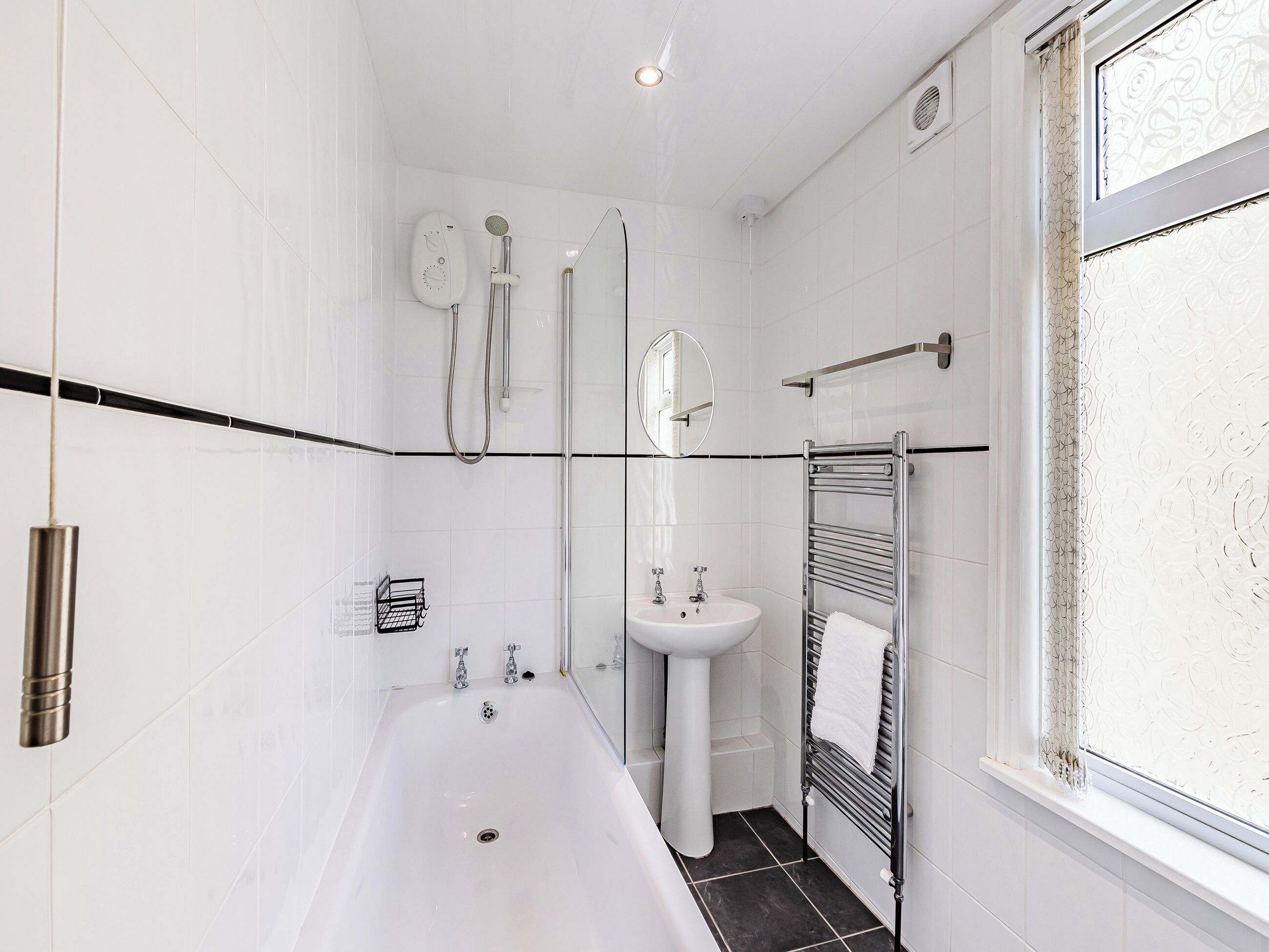 A modern bathroom with a bathtub, a pedestal sink, a glass shower enclosure, and a towel rack.