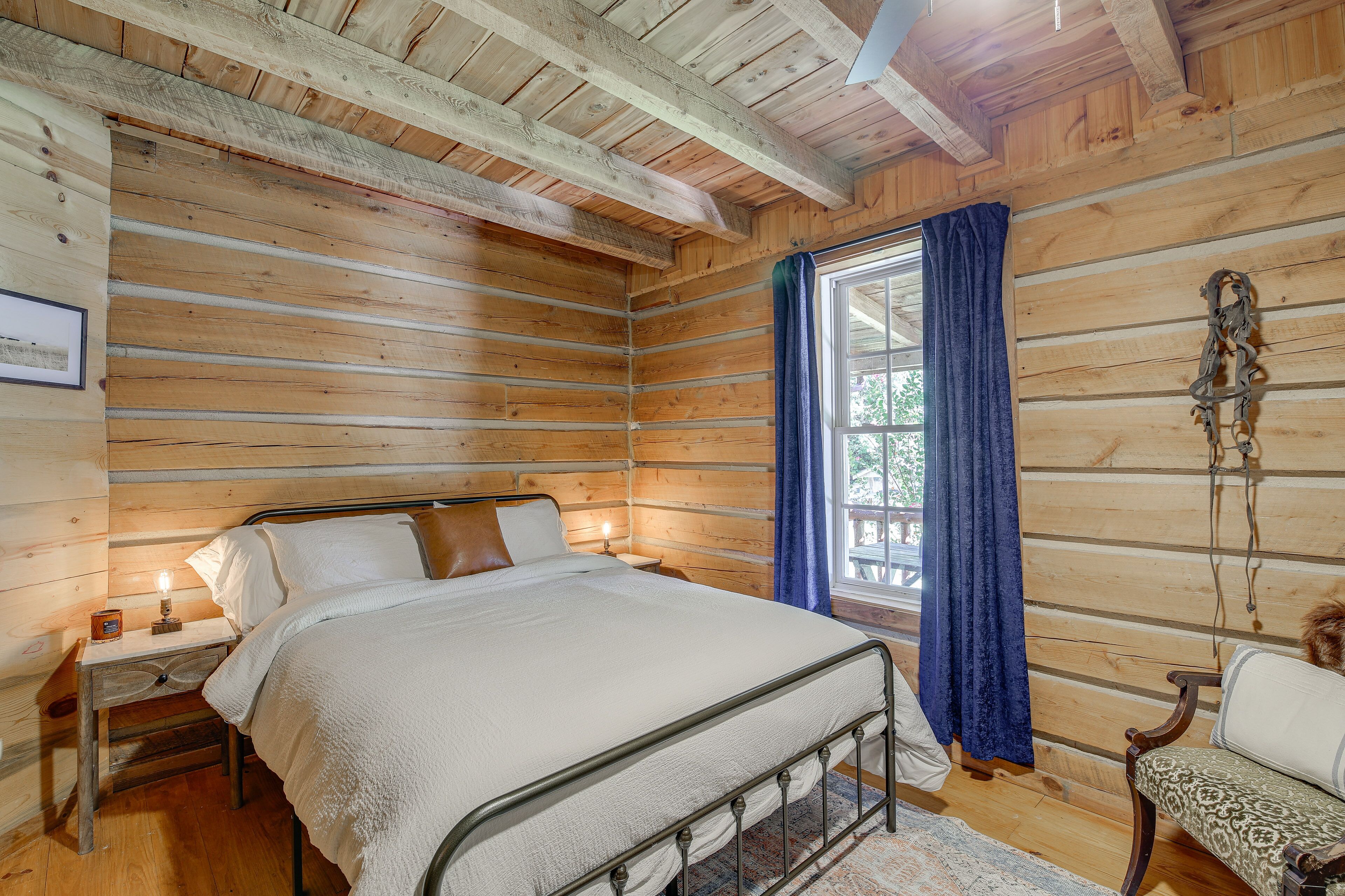 A wooden cabin bedroom with a bed, nightstands, and a window with curtains.