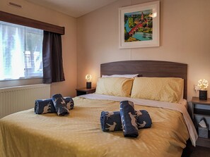 Una habitación de hotel con una cama, dos mesitas de noche con lámparas, una ventana con cortinas y un cuadro en la pared.