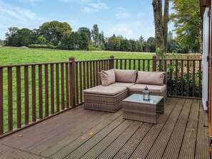 Um terraço com um sofá de vime e uma mesa de vidro, com vista para um campo gramado.
