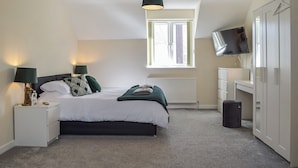 A bedroom with a bed, bedside lamps, a window, a radiator, a TV, and a wardrobe.