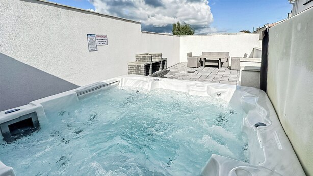 A hot tub with a tiled patio area, a sign indicating spa rules, and a seating area with a table and chairs.