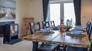 A dining area with a wooden table set for four, surrounded by chairs, a fireplace, and a view of the outdoors.
