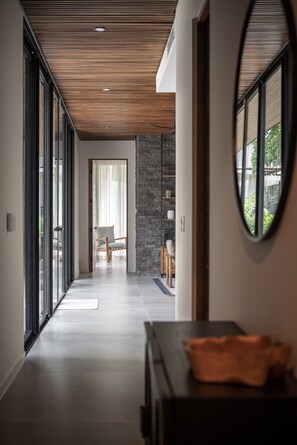 Ein moderner Flur mit Holzbalkendecke, Steinwand und Blick auf einen Balkon mit einem Sessel.