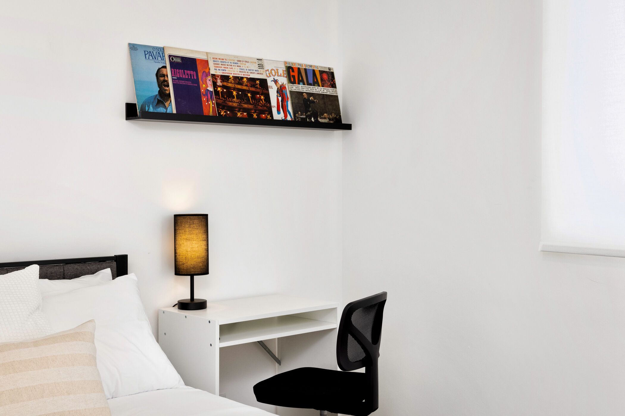 A bedroom with a bed, a desk with a chair, a lamp, and a wall-mounted artwork.