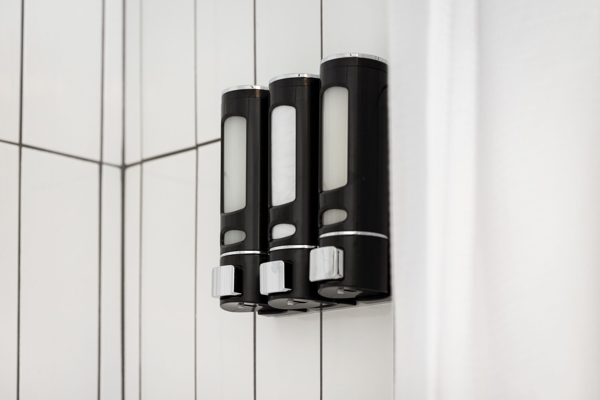 Trois objets cylindriques noirs, fixés sur un mur blanc orné d’un motif géométrique.