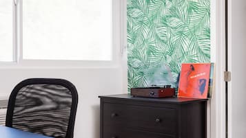 Una habitación con ventana, una silla, un escritorio, un aparador oscuro y una pared con estampado de hojas verdes.