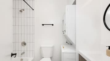 A bathroom with a white tiled shower, a toilet, a sink, and a mirror.