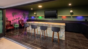 A bar area with a counter, stools, a television, and a mural of palm trees. - Fenix Hotel Hollywood (Los Angeles)