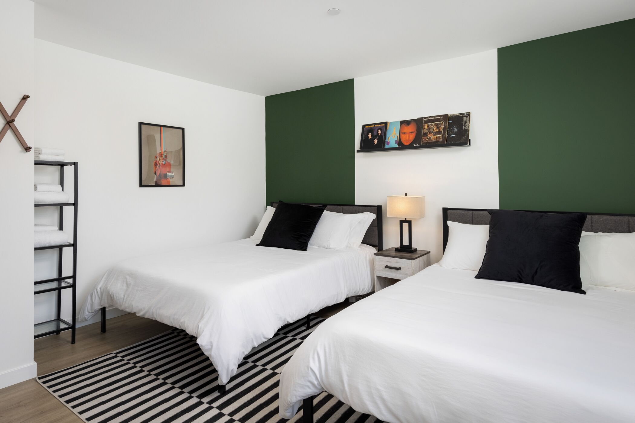 A hotel room with two beds, a black and white striped rug, a wall-mounted shelf, and a framed picture.
