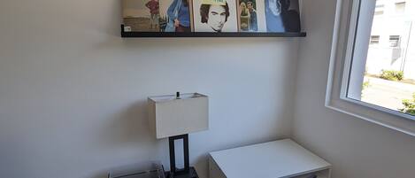 A small office space with a desk, chair, lamp, and a wall-mounted shelf with framed pictures.