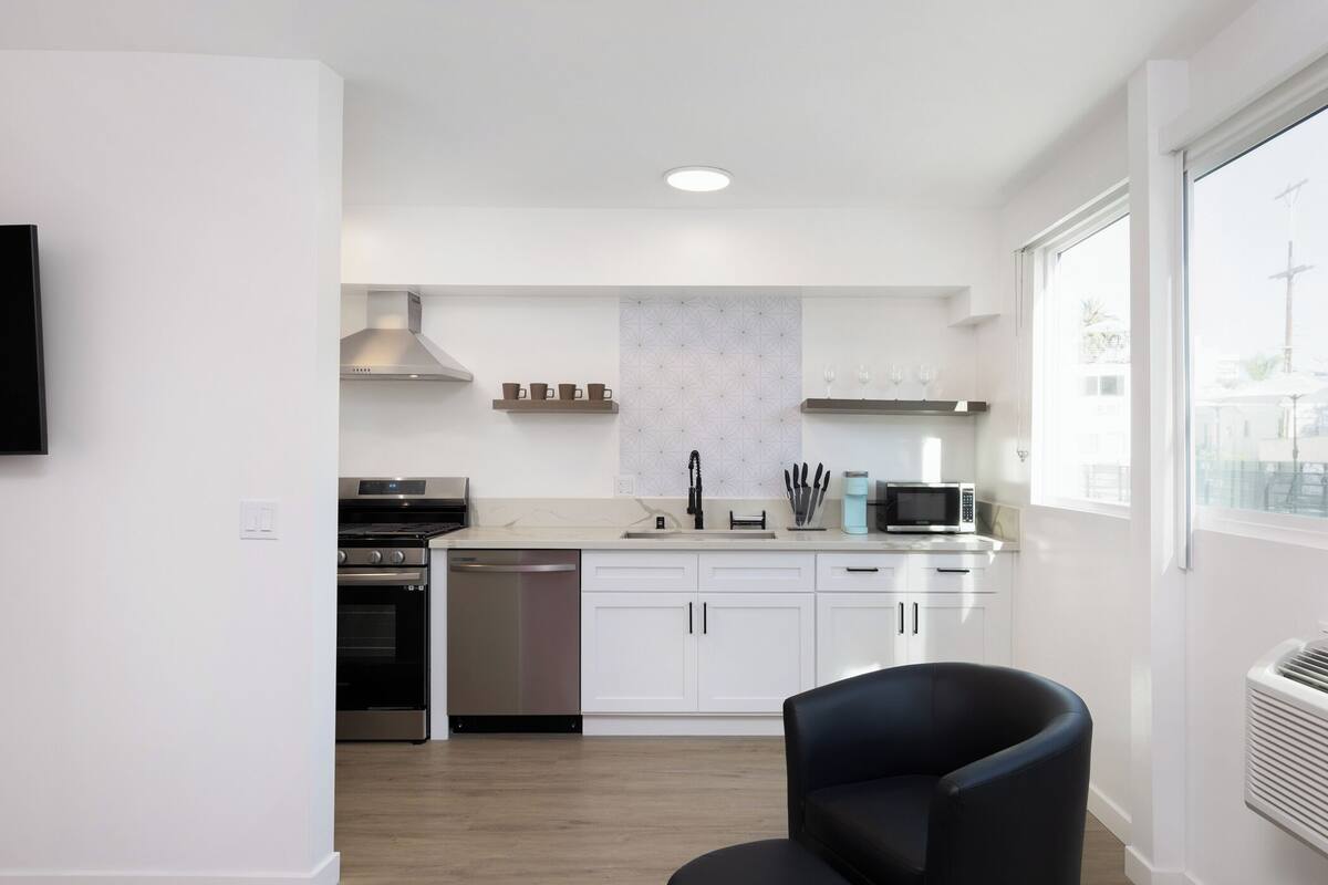 A modern kitchen with white cabinets, stainless steel appliances, and a black chair.