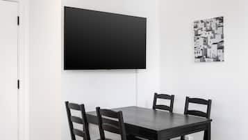 A dining area with a dark wooden table and four chairs, a flat-screen TV mounted on the wall, and a black and white patterned artwork on the wall.