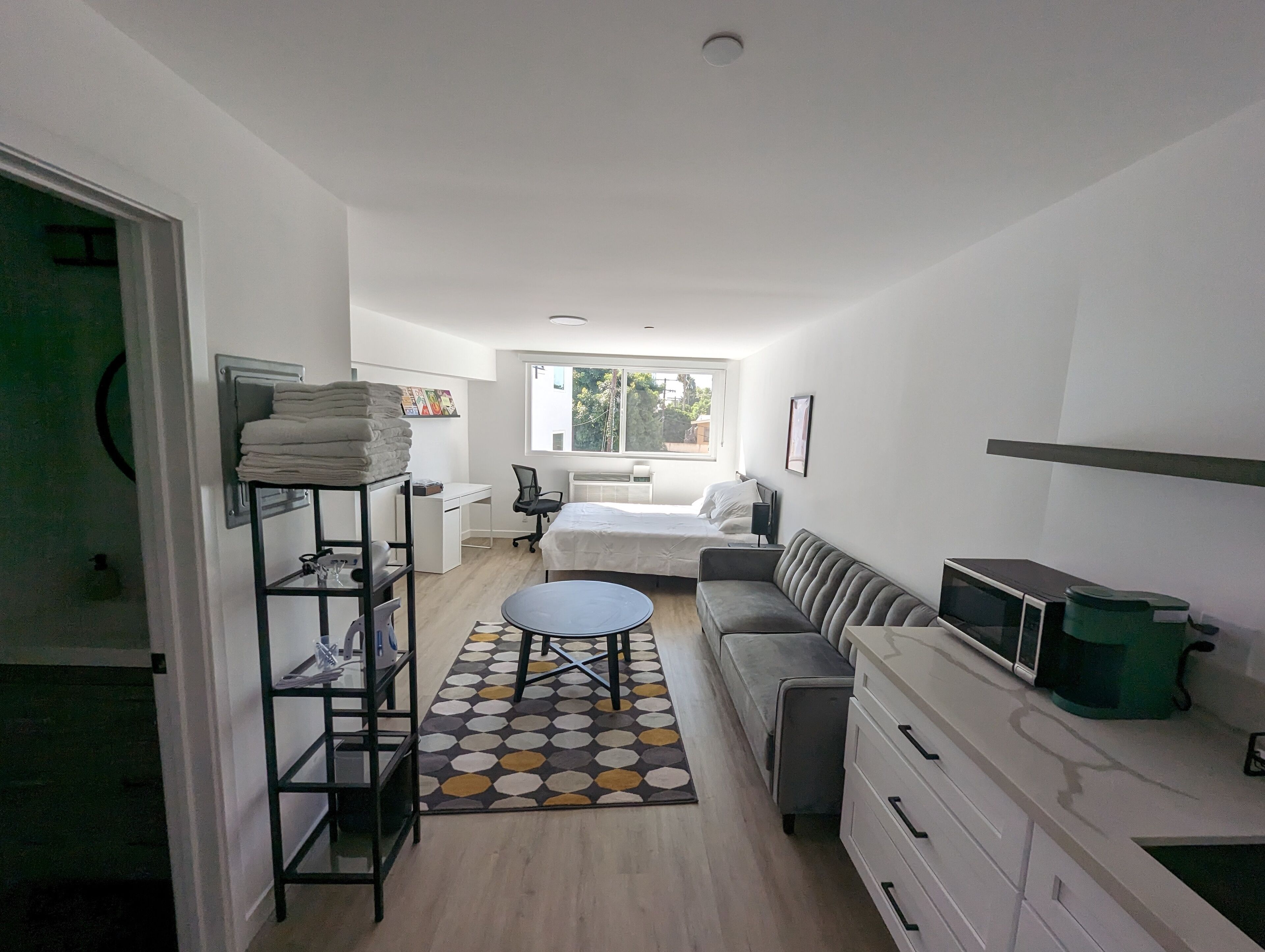 A compact hotel room with a bed, a sofa, a desk, and a small kitchenette.