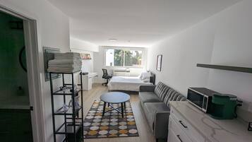 A compact hotel room with a bed, a sofa, a desk, and a small kitchenette.