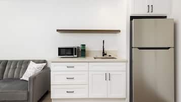 A compact kitchen with a grey sofa, white cabinets, a microwave, and a stainless steel refrigerator.