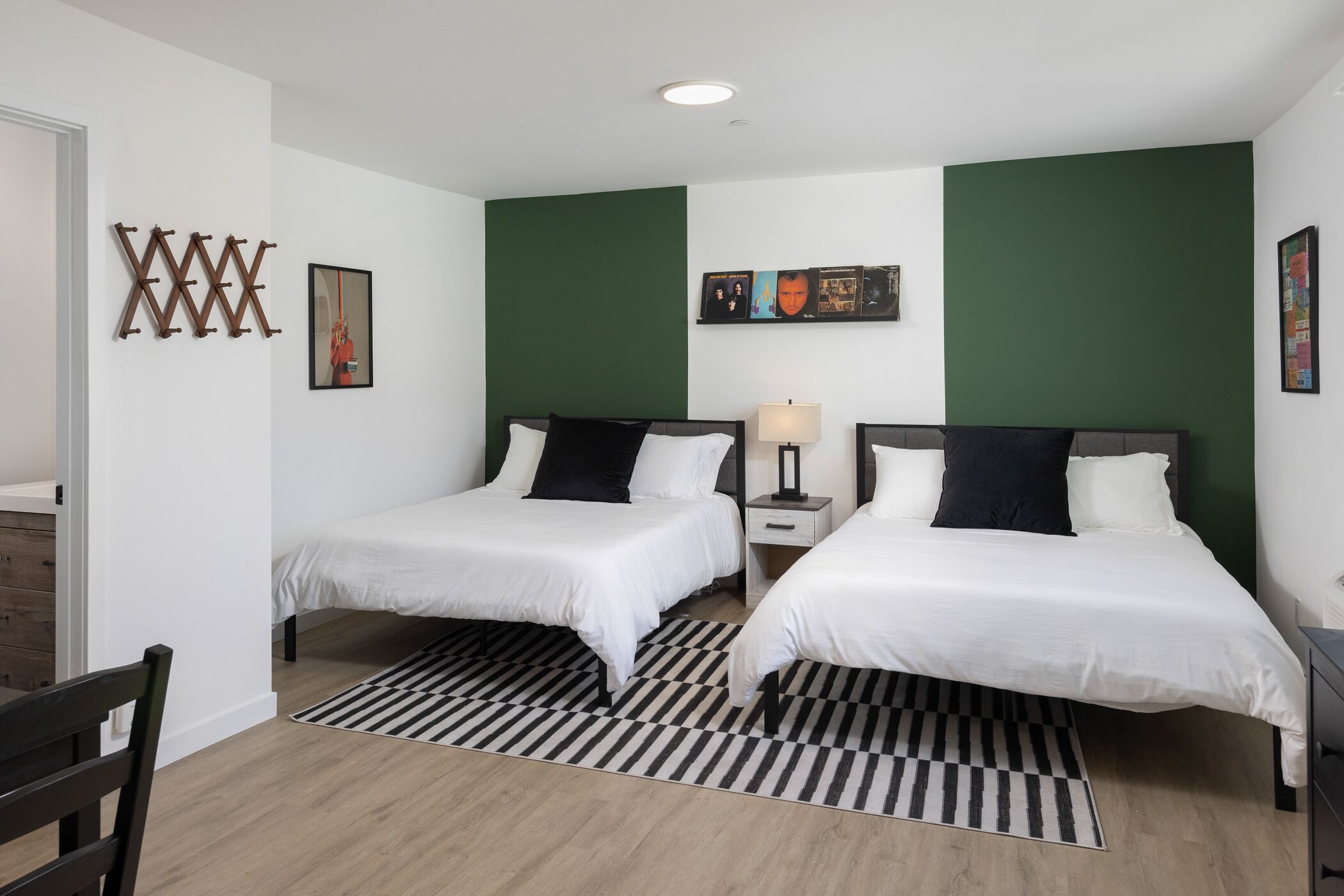 Een hotelkamer met twee bedden, een zwart-wit gestreept tapijt, een groene accentmuur en een kleine tafel met een lamp.