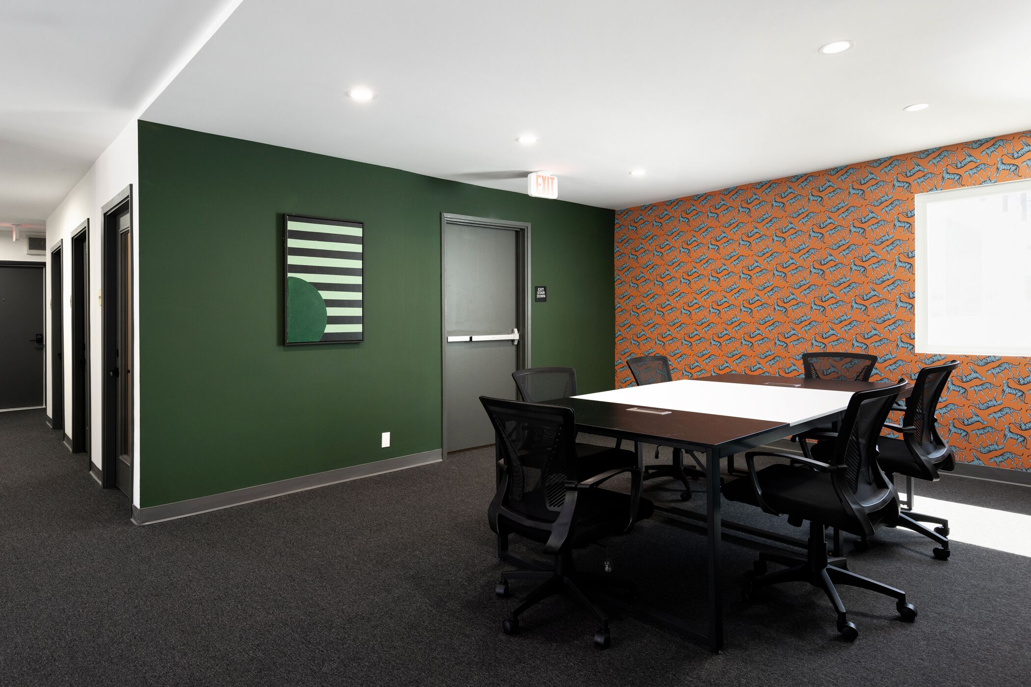 Une salle de conférence avec une longue table, des chaises noires, des murs verts et un papier peint à motifs.