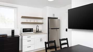 A modern kitchen with white cabinets, a stainless steel refrigerator, a microwave, and a black dining table with chairs.