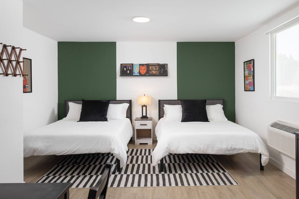 A modern hotel room with two beds, a black and white striped rug, a small table, and a wall-mounted artwork.