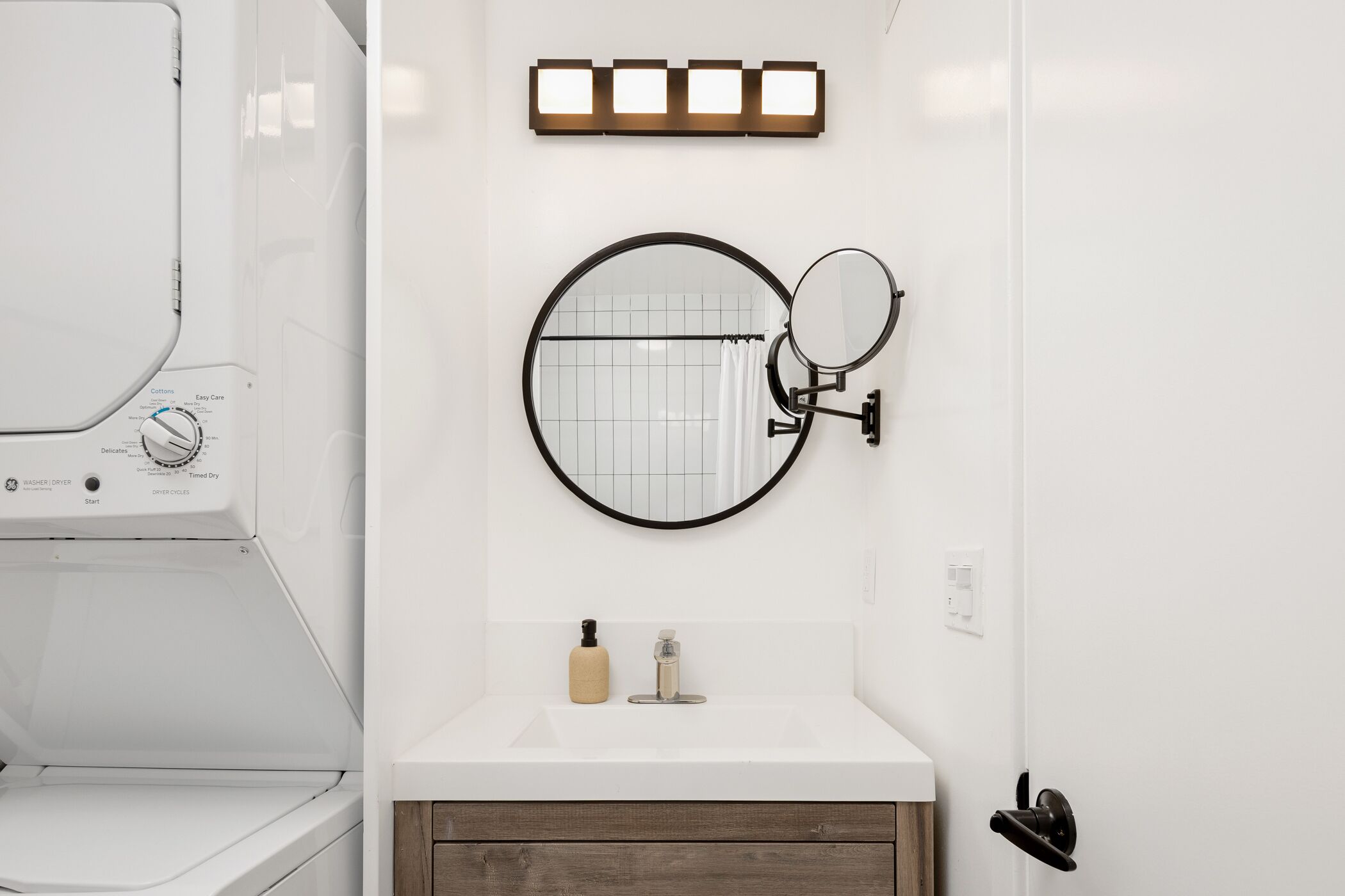 Une salle de bain moderne avec un lavabo blanc, un miroir rond, un porte-serviettes et un lave-linge encastré.