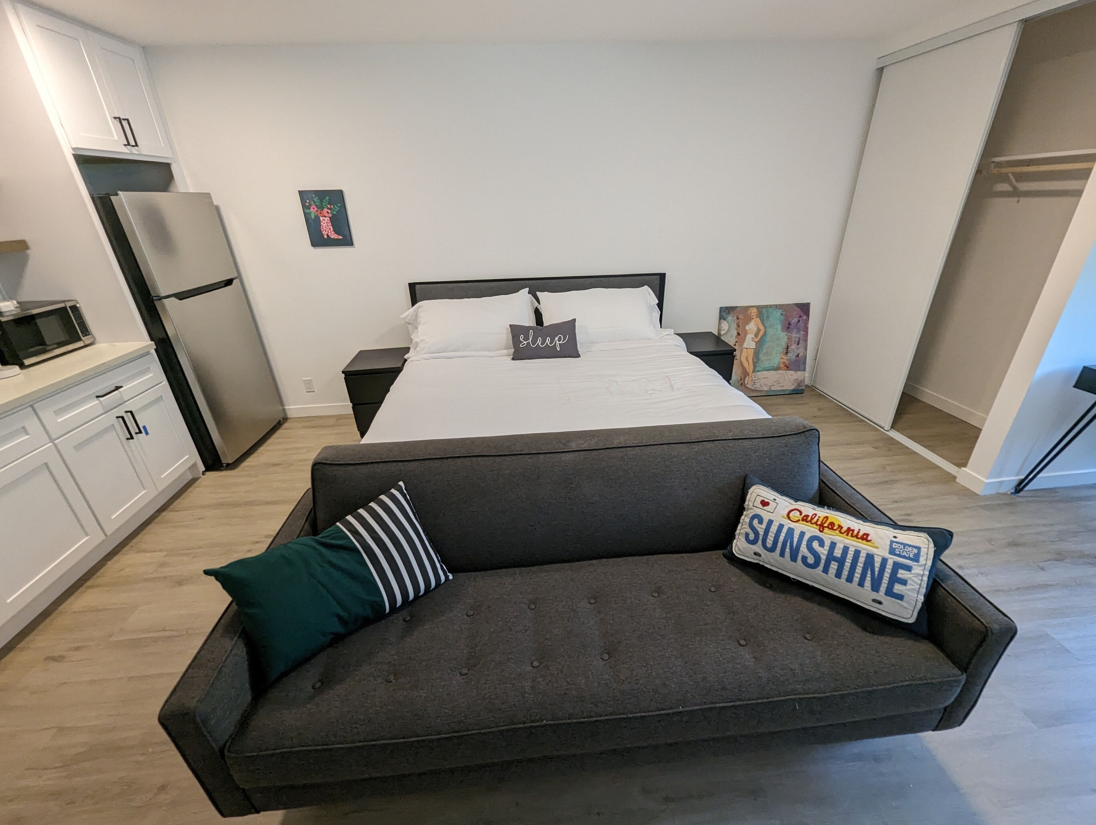 A modern bedroom with a bed, a sofa, a refrigerator, a microwave, and a painting on the wall.