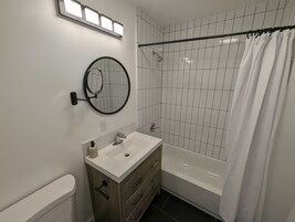 Un baño moderno con lavamanos, tocador y bañera blancos.