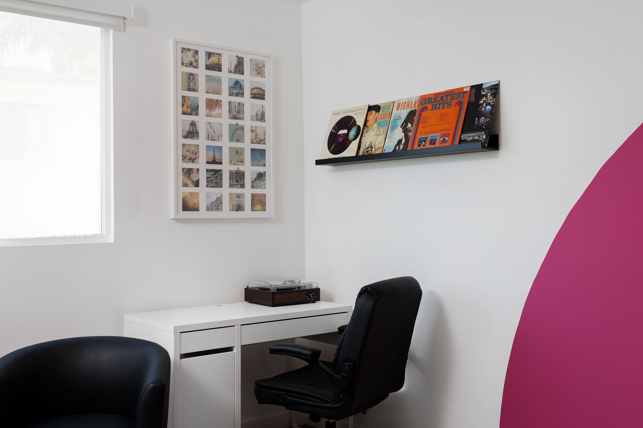 Una habitación con un escritorio blanco, una silla de oficina negra y una estantería de pared con discos de vinilo.