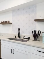 Una cucina moderna con un lavello doppio, mobili bianchi e uno schienale decorato.