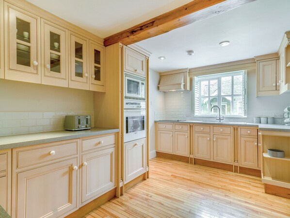A kitchen with wooden cabinets, a built-in oven, a microwave, and a window with a view of the outside.