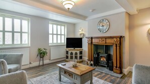 A living room with a fireplace, a television, and a clock on the wall. - 2 bedroom accommodation in Willoughton (Willoughton)