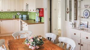 A kitchen with white cabinets, a green backsplash, and a wooden dining table with chairs. - 3 bedroom accommodation in Pentraeth (Pentraeth)