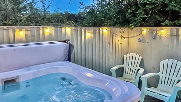 A hot tub with a wooden deck, surrounded by white plastic chairs and string lights. - 3 bedroom accommodation in Pentraeth (Pentraeth)