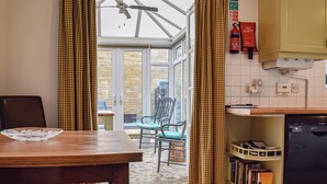 Une cuisine avec un coin repas, une fenêtre avec des rideaux, un ventilateur de plafond et un extincteur.
