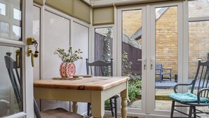 Une véranda avec une table en bois, des chaises et une plante en pot.