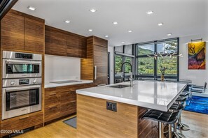 Eine moderne Küche mit eingebauten Geräten, einer großen Kochinsel inklusive Barhocker und Blick auf eine Berglandschaft durch große Fenster.
