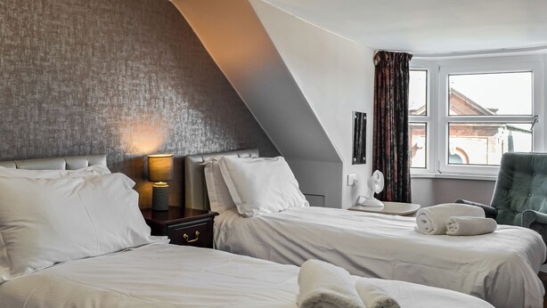 A hotel room with two beds, a bedside table with a lamp, a chair, and a window with curtains. - 3 bedroom accommodation in Castle Douglas (Castle Douglas)