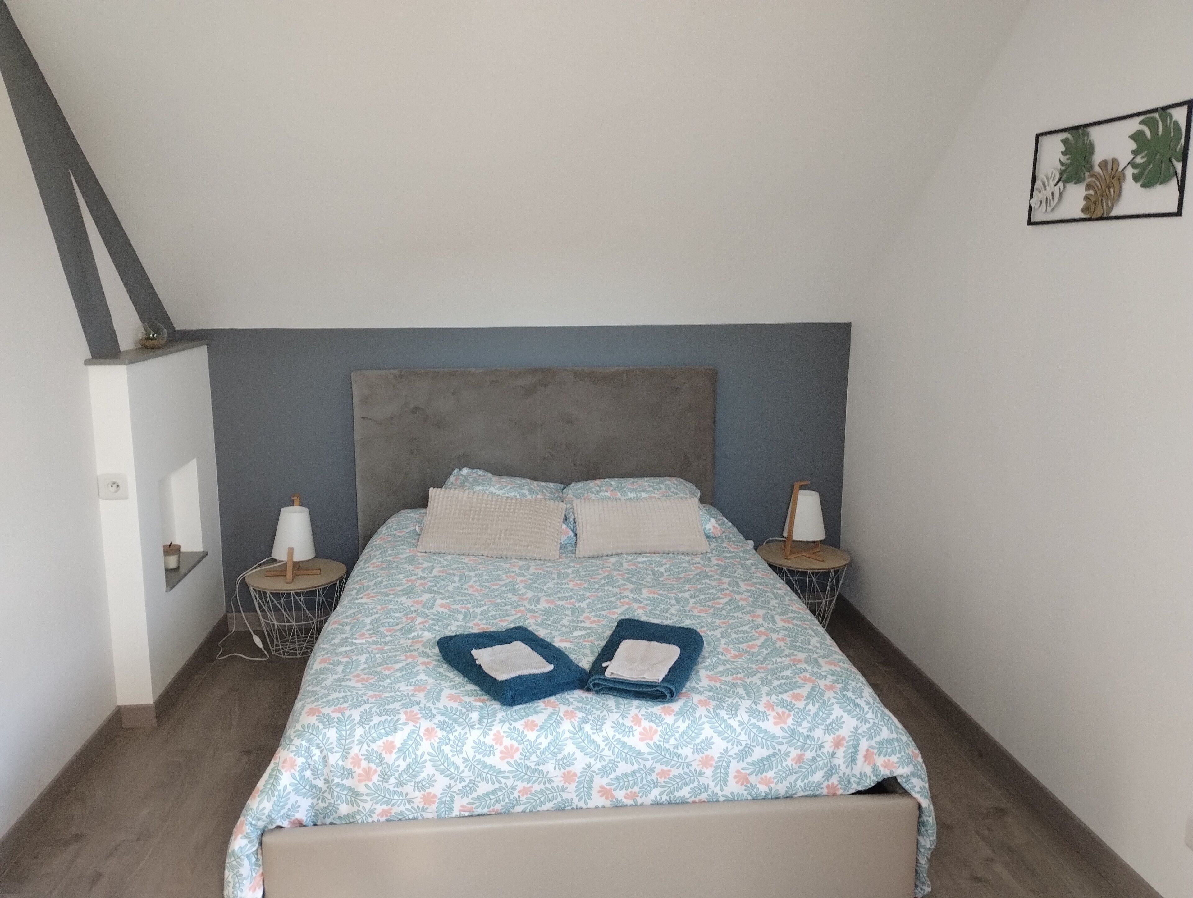Un dormitorio con cama, dos mesitas de noche, cabecero y una planta colgante en la pared.