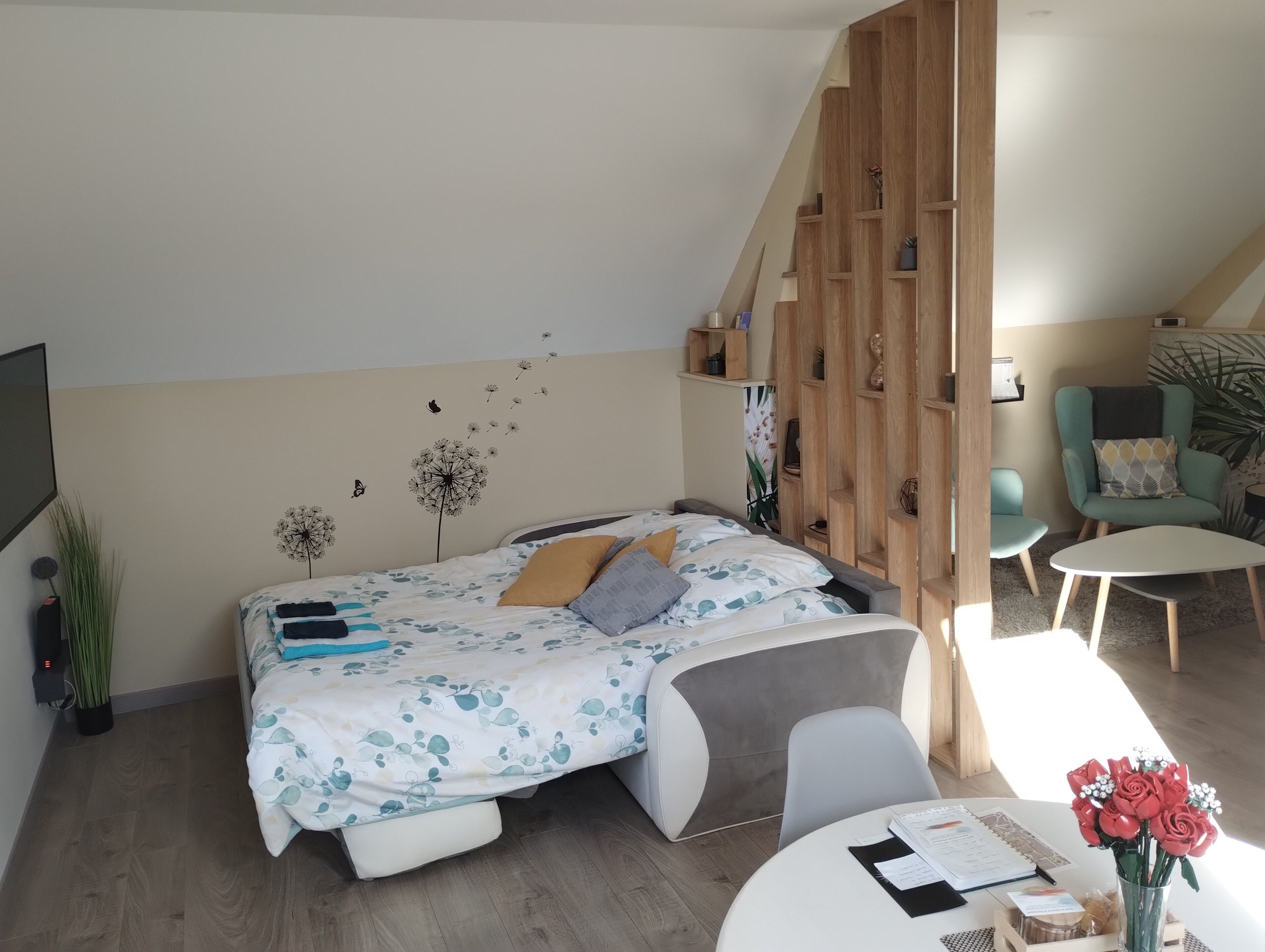 Een moderne slaapkamer met een bed, een bureau en een stoel. Er is een houten wandplank en een plant op de vloer.