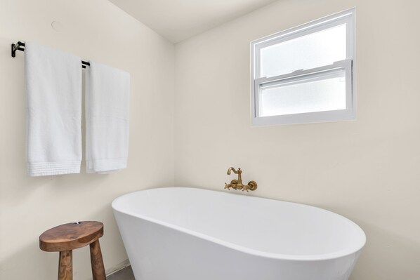 Un baño con una bañera independiente, un taburete de madera y dos toallas colgadas en un perchero.