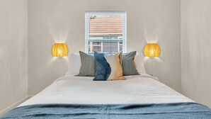 A bedroom with a bed, two wall-mounted lamps, a window with blinds, and a view of buildings outside. - Discounted long stays- Located near St Pete beaches, downtown Gulfport (Gulfport)