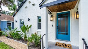 A white building with a blue door, a 'hello' mat, and a small garden with plants and a gravel path. - Discounted long stays- Located near St Pete beaches, downtown Gulfport (Gulfport)