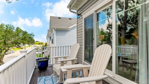 Eine überdachte Veranda mit weißen Adirondack-Stühlen, einem blauen Teppich und einem großen Fenster, in dem sich ein Baum spiegelt.