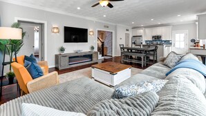 Ein geräumiges Wohnzimmer mit Kamin, einer großen Couch, einem Couchtisch und einem Essbereich, mit einer Küche im Hintergrund.