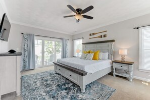 A bedroom with a bed, a ceiling fan, a nightstand, a TV, and a window with curtains.