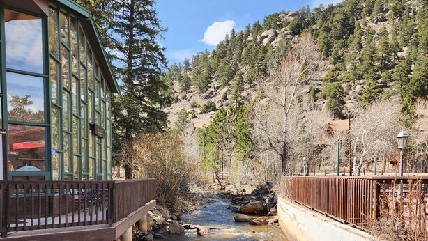 A bridge over a clear stream with a building on the left. - Spacious Lower-Level Hotel Queen and Full-size beds with Views 108-110 (Estes Park)
