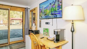 A hotel room with a wooden desk, a television mounted on the wall, a coffee maker, a lamp, and a sliding glass door leading to an outdoor area. - Spacious Lower-Level Hotel Queen and Full-size beds with Views 108-110 (Estes Park)