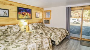 A room with two beds, a wooden wall, a painting, and a window with a view of a car outside. - Spacious Lower-Level Hotel Queen and Full-size beds with Views 108-110 (Estes Park)